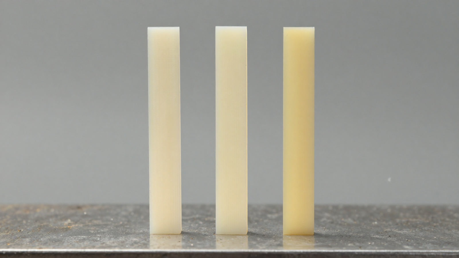 三根浅色薄条竖排站在钢板上，厚度依次不同，侧光把每根的边缘勾出来。